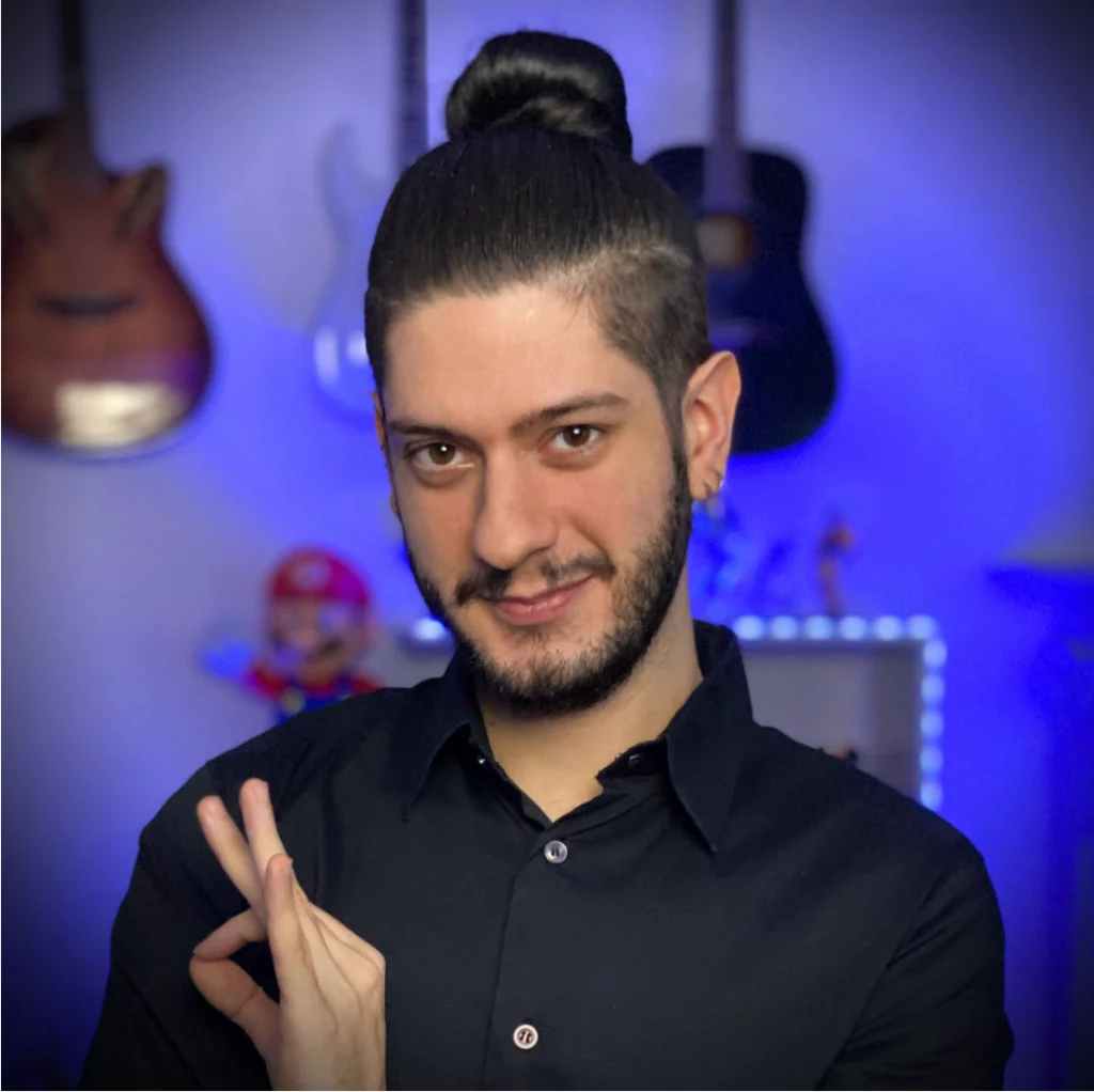Uomo con capelli raccolti in uno studio con strumenti musicali sullo sfondo.