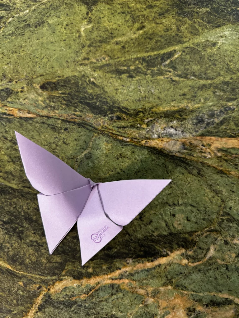 Farfalla origami di colore lilla su sfondo di marmo verde, con il logo della Fondazione Italiana Epilessia visibile sull'ala.